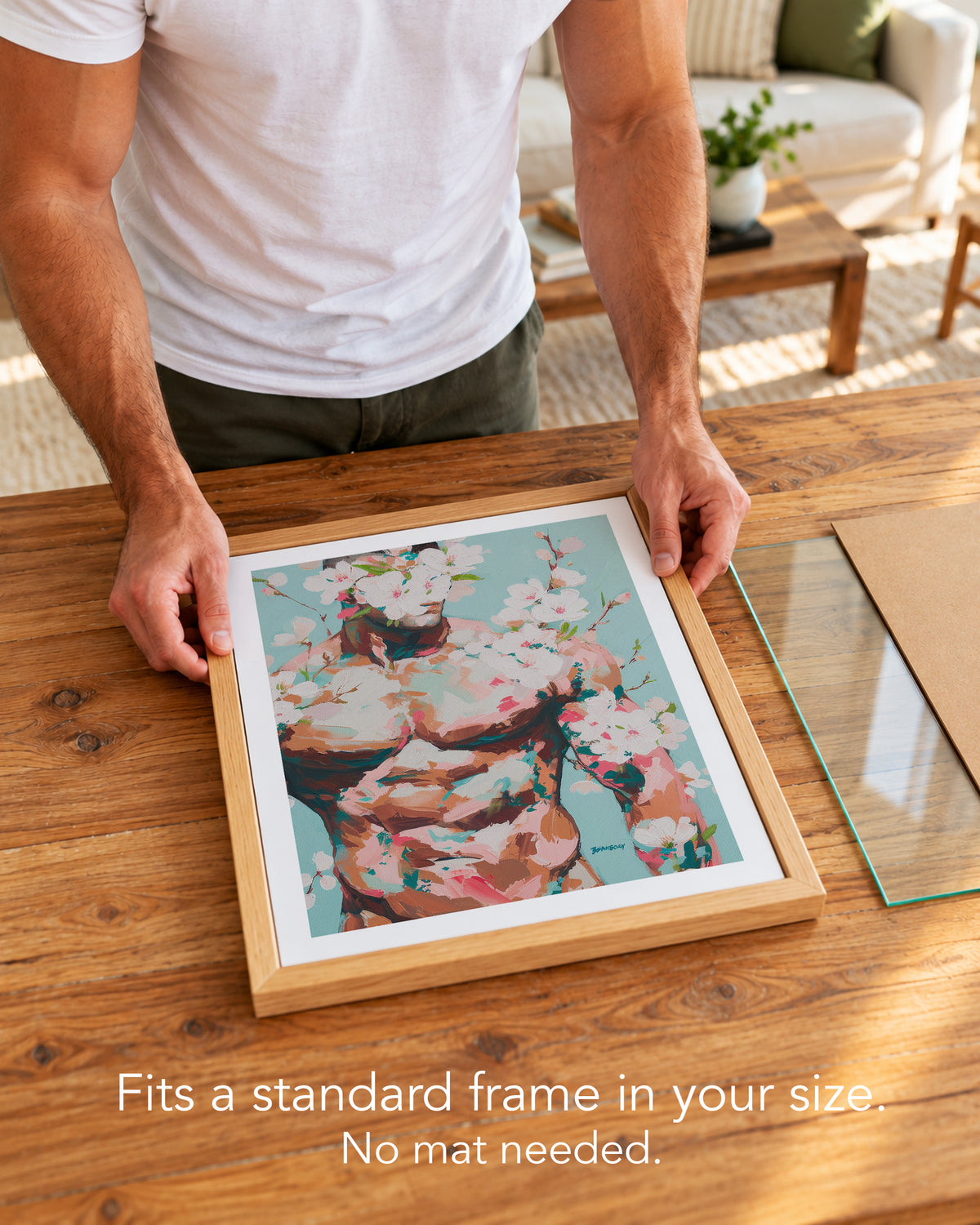 A man placing the Quiet Orchard paper art print with a white border into a standard wood frame, no mat needed