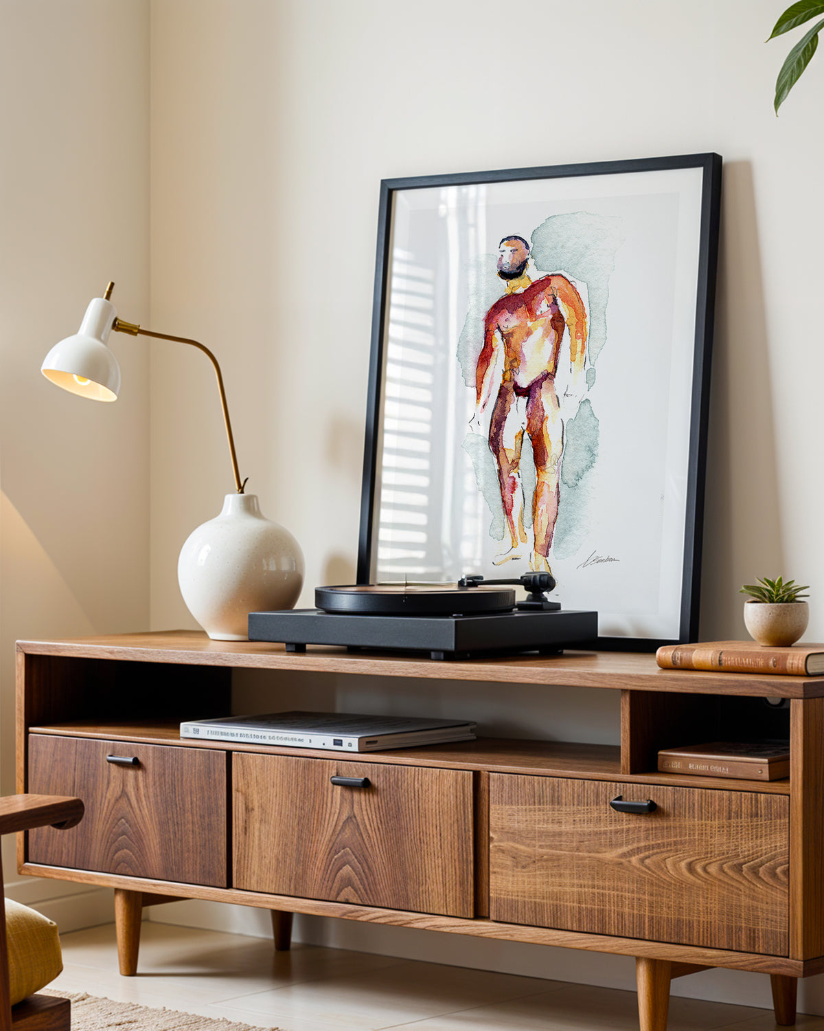 Heavyweight art print in a black frame leaning on a walnut sideboard beside a record player
