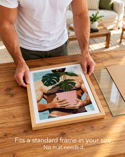 A man placing the Small Jungle paper art print with a white border into a standard wood frame, no mat needed