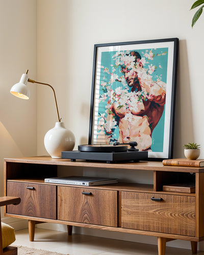 Soft Riot art print in a black frame leaning on a walnut sideboard beside a record player