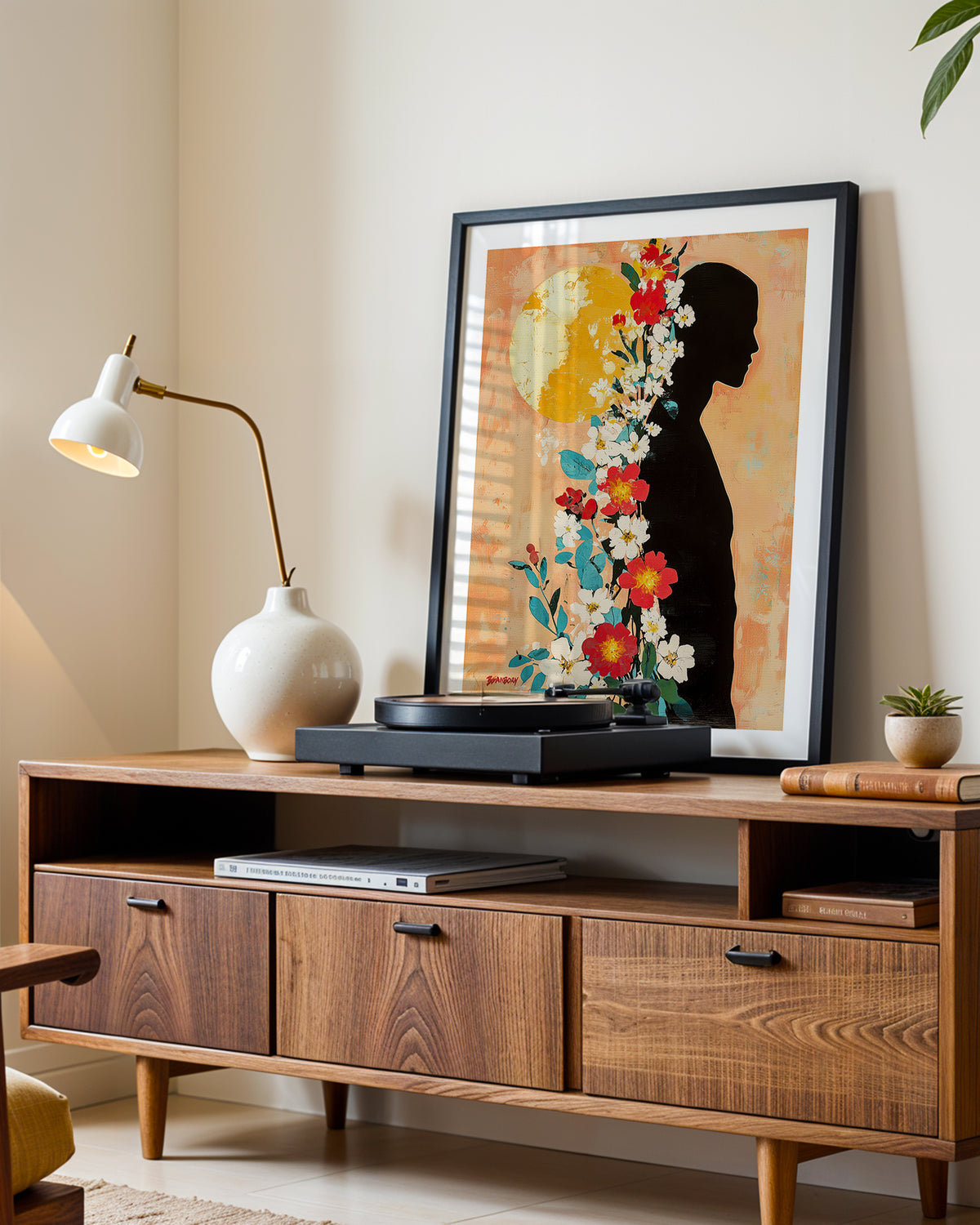 Sun Keeper art print in a black frame leaning on a walnut sideboard beside a record player