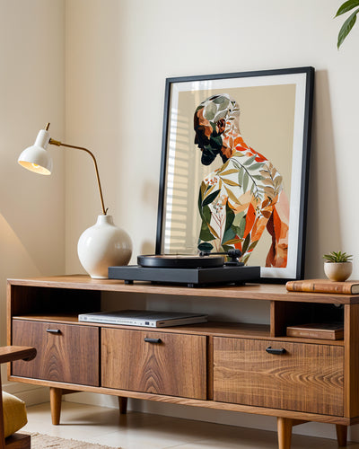 Turning Leaf art print in a black frame leaning on a walnut sideboard beside a record player