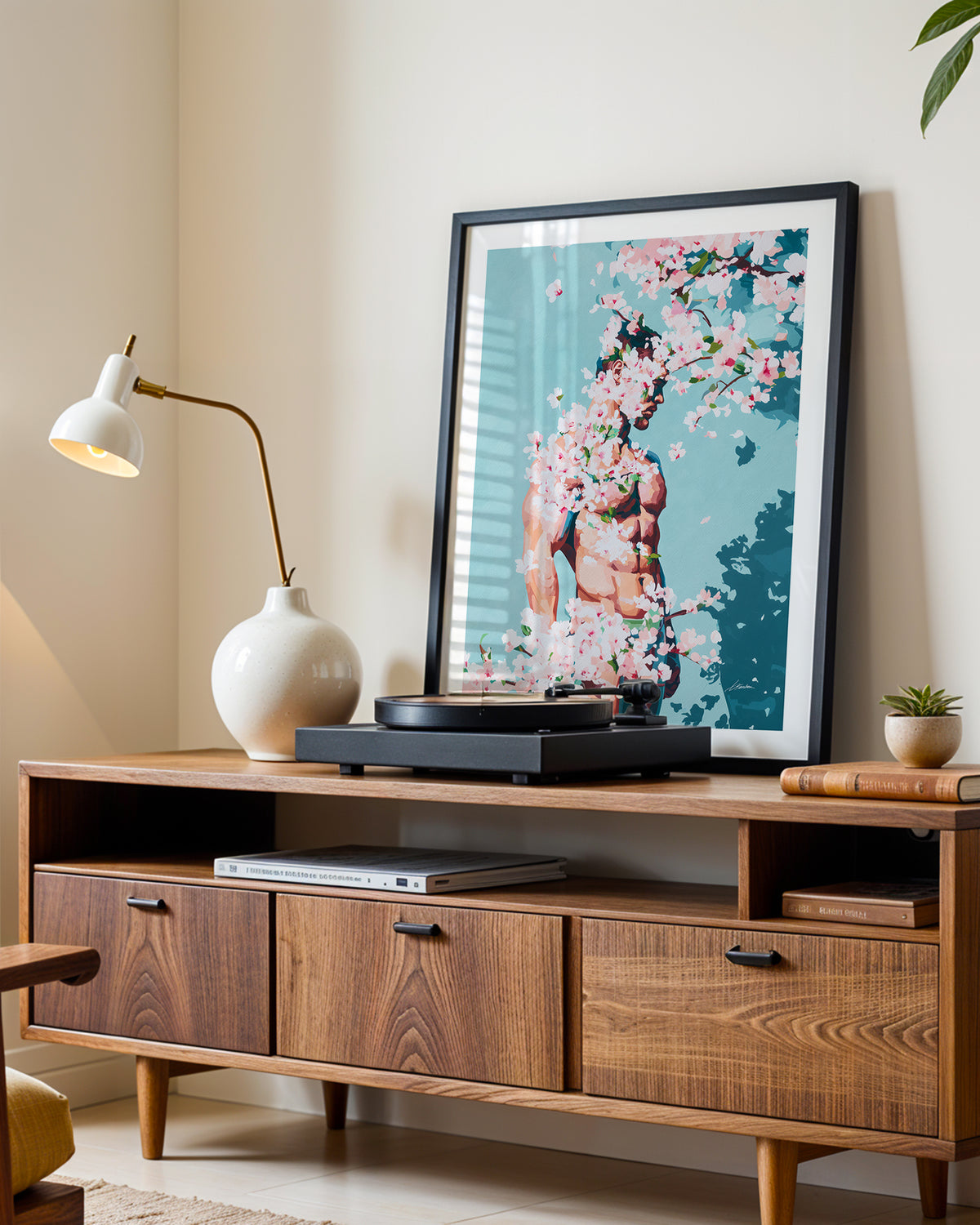 Under Branches art print in a black frame leaning on a walnut sideboard beside a record player