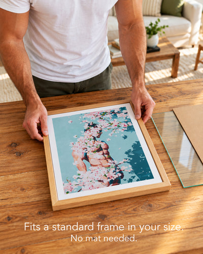 A man placing the Under Branches paper art print with a white border into a standard wood frame, no mat needed
